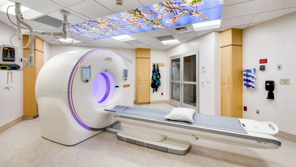 Hospital imaging room with a CT scanner, patient table, and a ceiling panel showing cherry blossoms
