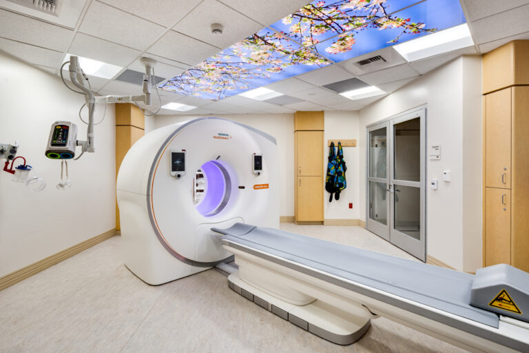 Hospital CT scanner room with a patient table and a ceiling panel showing flowering branches and blue sky