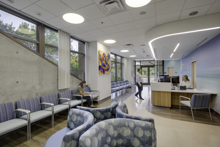 Modern medical clinic waiting room with seating, reception desk, and people waiting or checking in