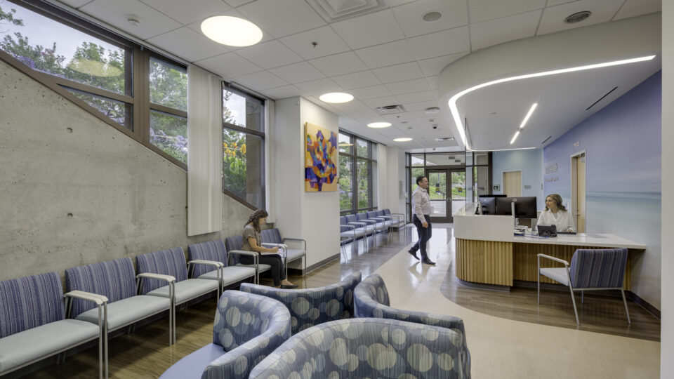 Modern medical clinic waiting room with seating, reception desk, and people waiting or checking in