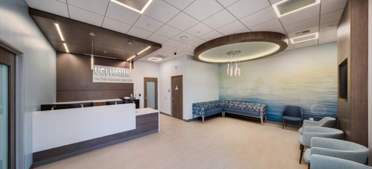 Modern medical clinic reception area with UCI Health signage, waiting chairs, and soft blue ocean wall mural