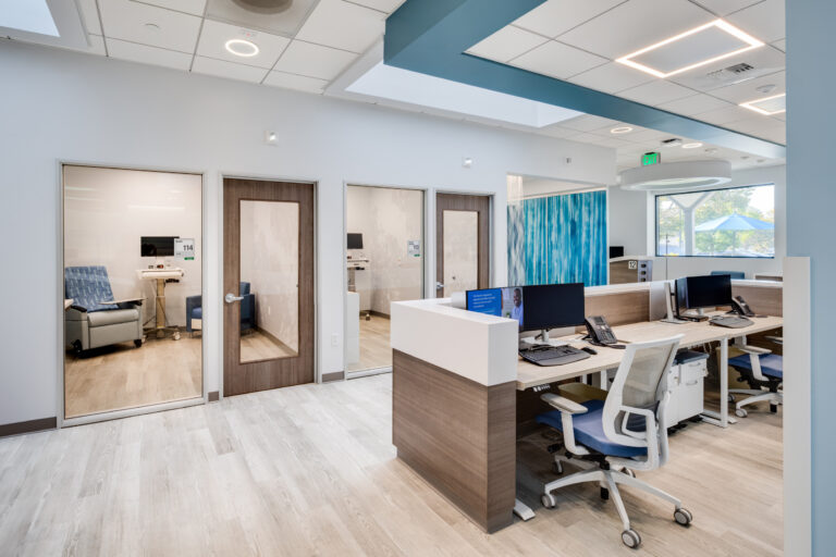 Modern medical clinic reception area with exam room doors, workstations, and bright ceiling lights