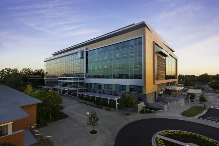 Modern glass office building at sunset with a courtyard and curved driveway