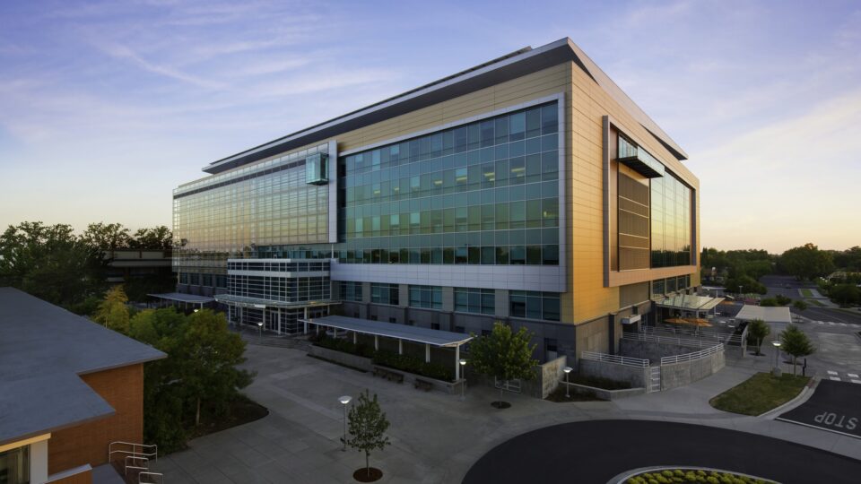 Modern glass office building at sunset with a courtyard and curved driveway