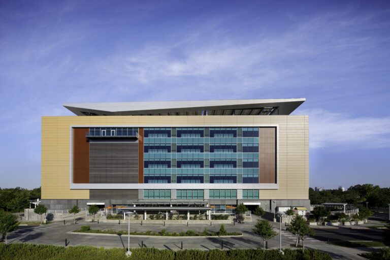Modern multi-story building with teal glass windows and a large angular roof under a blue sky