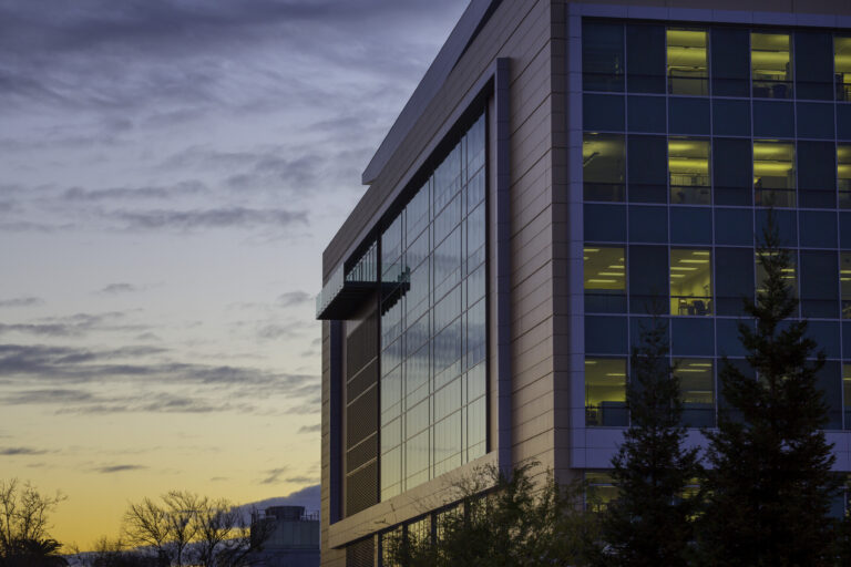 Modern office building at dusk with lit windows against a cloudy sunset sky