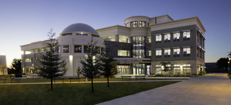 Modern science center and museum building at dusk with a dome, lit windows, and a curved walkway in front