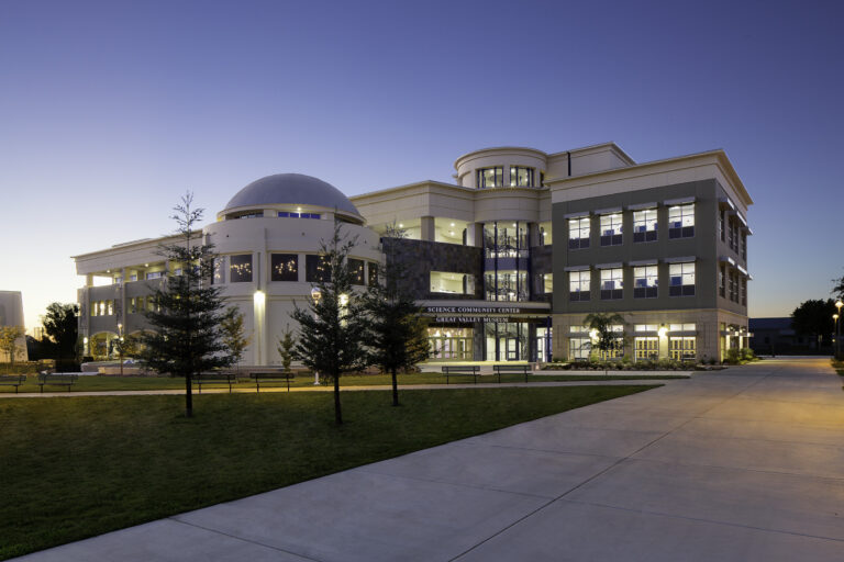 Modern science center and museum building at dusk with a dome, lit windows, and a curved walkway in front