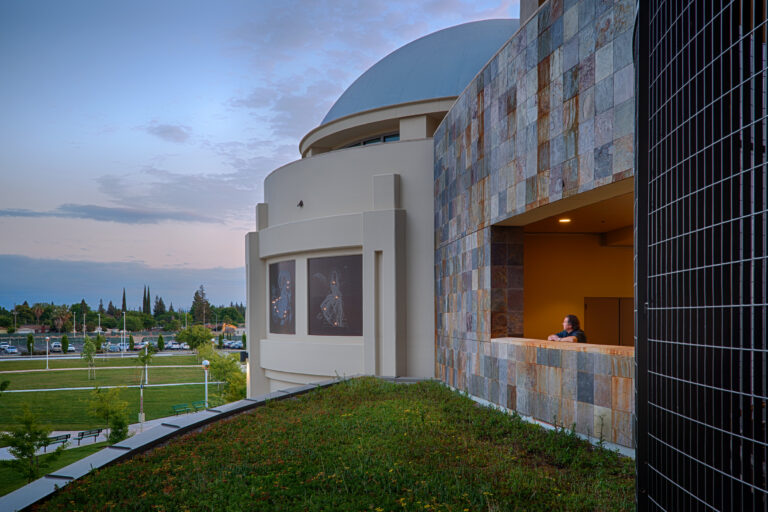 Modern building with a dome, stone facade, and a man leaning on a balcony at dusk
