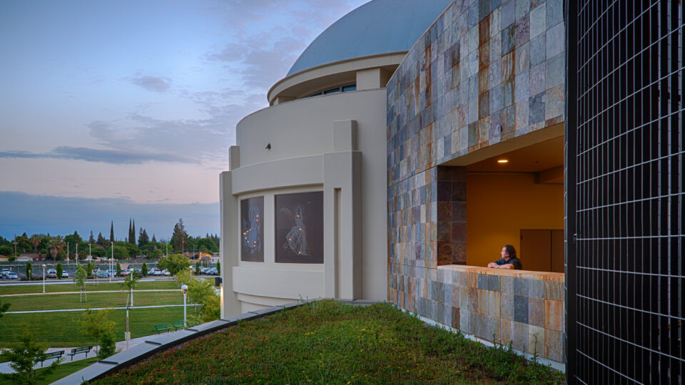 Modern building with a dome, stone facade, and a man leaning on a balcony at dusk