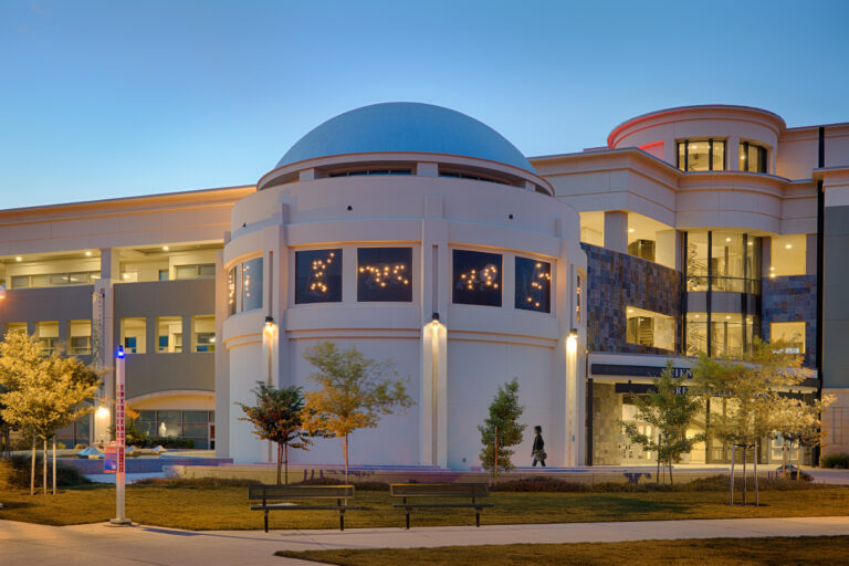 Modern campus building with a large blue dome and lit windows at dusk