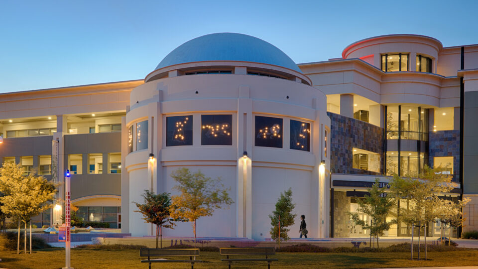 Modern campus building with a large blue dome and lit windows at dusk