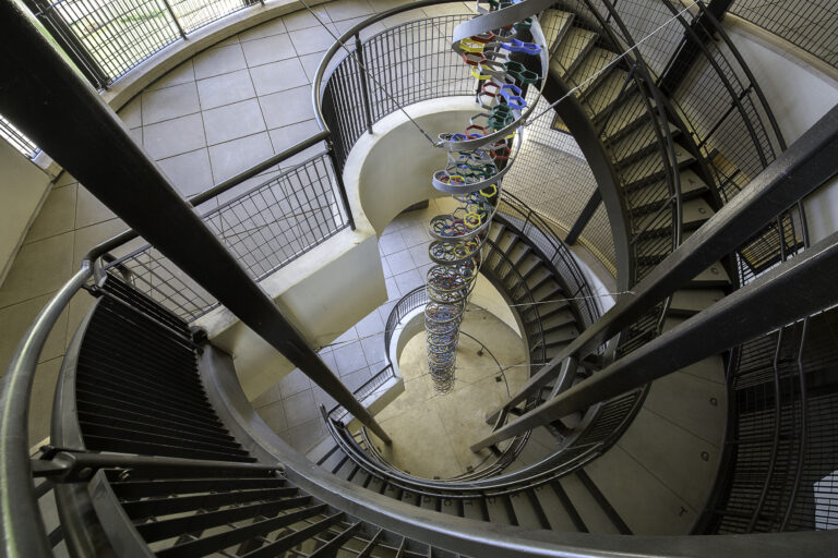 Top-down view of a spiral staircase with metal railings and a colorful hanging helix sculpture in the center