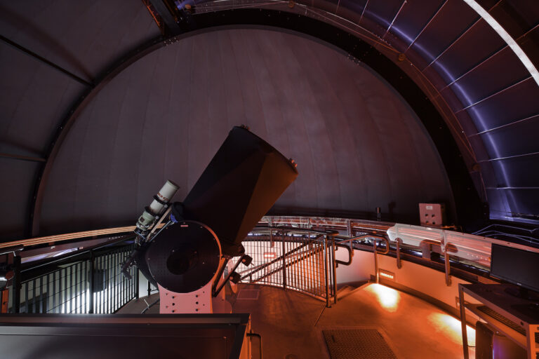 Large telescope inside a domed observatory, lit by red lighting
