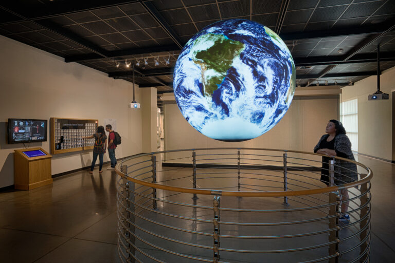 Museum exhibit with a large suspended glowing Earth globe and visitors viewing displays