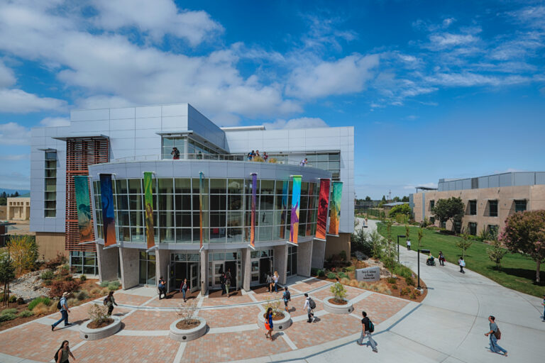 Modern campus building with colorful banners and students walking beneath a bright blue sky