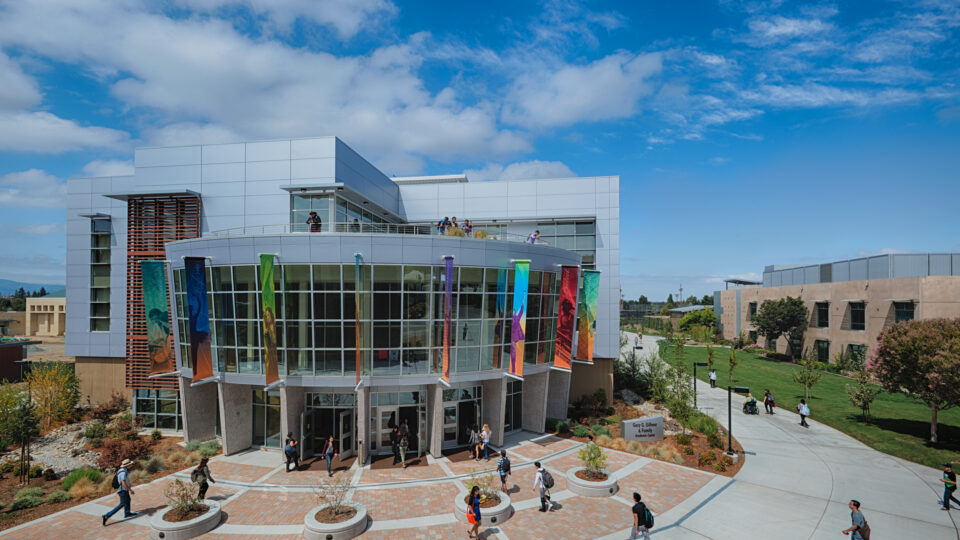 Modern campus building with colorful banners and students walking beneath a bright blue sky