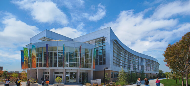 Modern curved campus building with glass front, colorful banners, and students walking under a blue sky