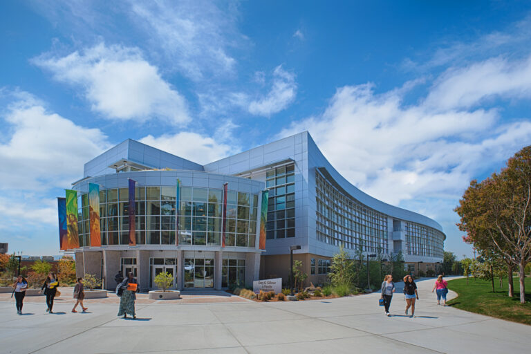 Modern curved campus building with glass front, colorful banners, and students walking under a blue sky