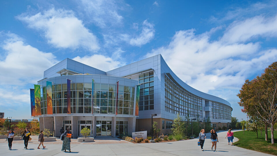 Modern curved campus building with glass front, colorful banners, and students walking under a blue sky