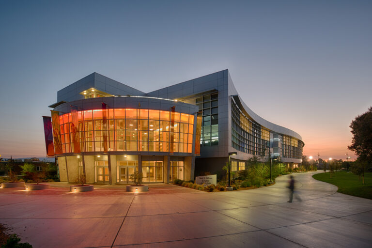 Modern curved building at dusk with glowing glass entrance and a winding walkway