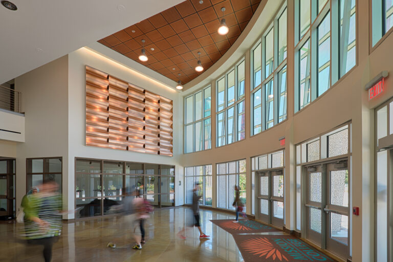 Bright modern lobby with tall windows, hanging lights, and people walking by an exit door