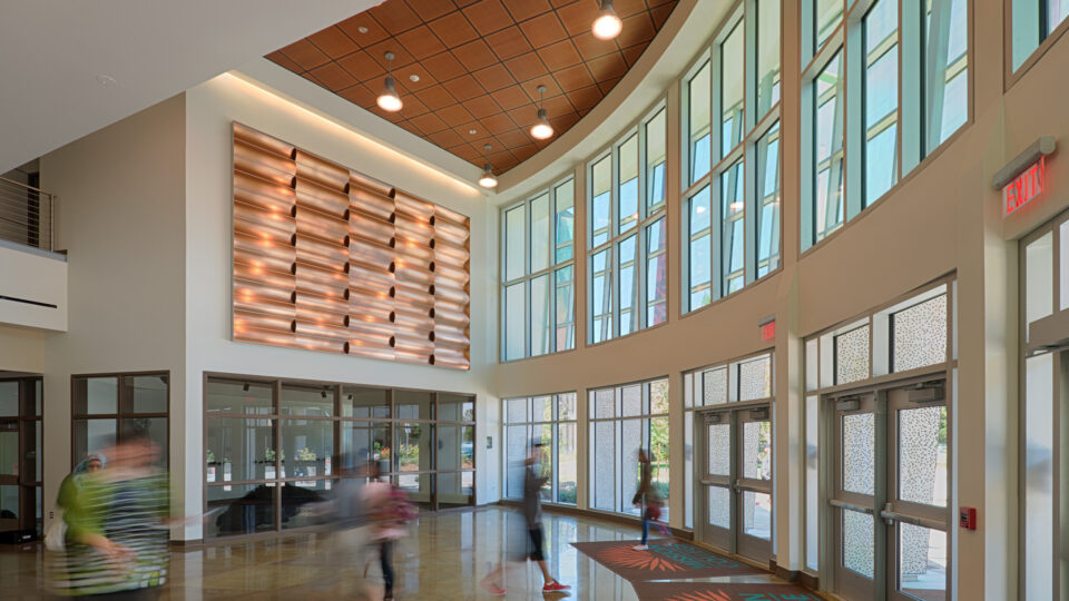 Bright modern lobby with tall windows, hanging lights, and people walking by an exit door