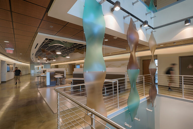 Modern hospital corridor with abstract hanging panels, railings, seating, and a few blurred people walking