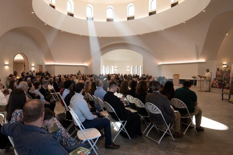 Congregation seated in a sunlit church dome during a service, with a priest at the altar