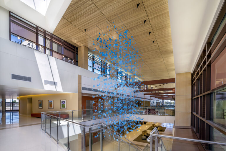 Modern atrium with skylights, glass railings, and a suspended blue abstract sculpture over stairs