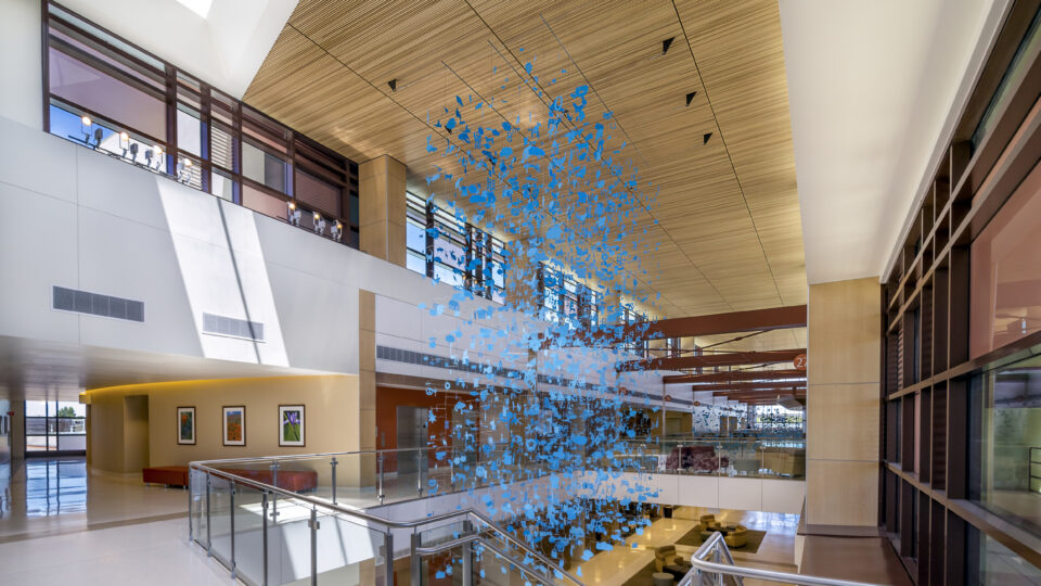 Modern atrium with skylights, glass railings, and a suspended blue abstract sculpture over stairs