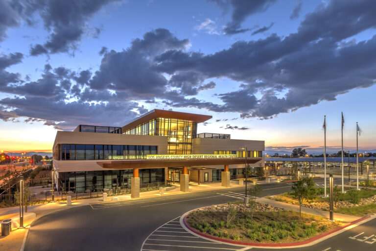 Modern hospital building at sunset with illuminated glass facade and a dramatic cloudy sky