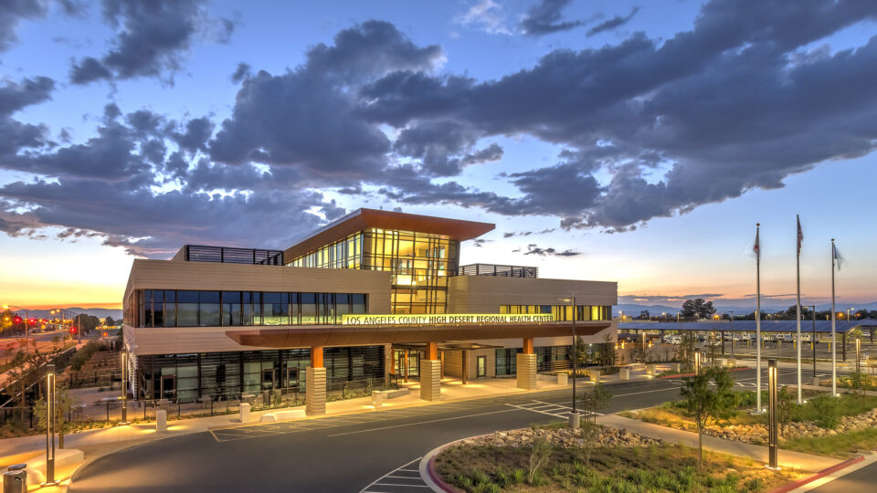 Modern hospital building at sunset with illuminated glass facade and a dramatic cloudy sky