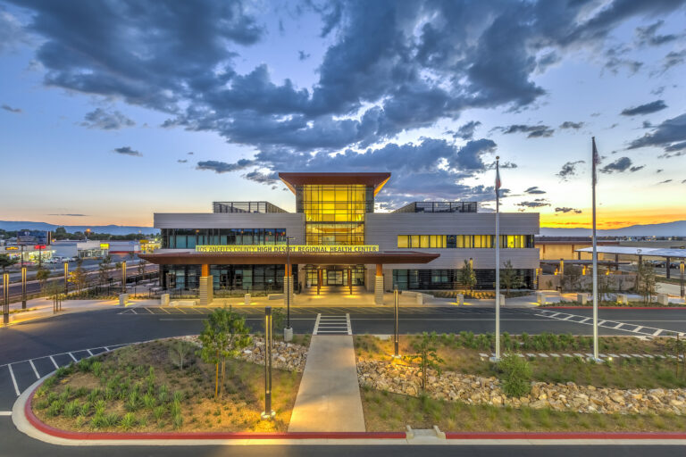 Modern health center building at sunset with glowing glass entrance and cloudy blue sky