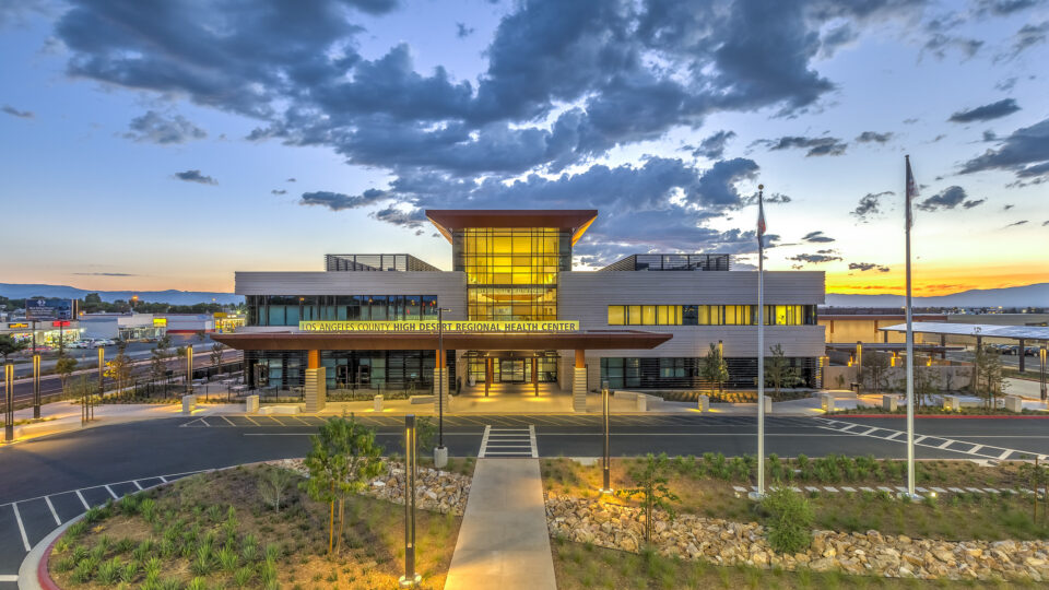 Modern health center building at sunset with glowing glass entrance and cloudy blue sky