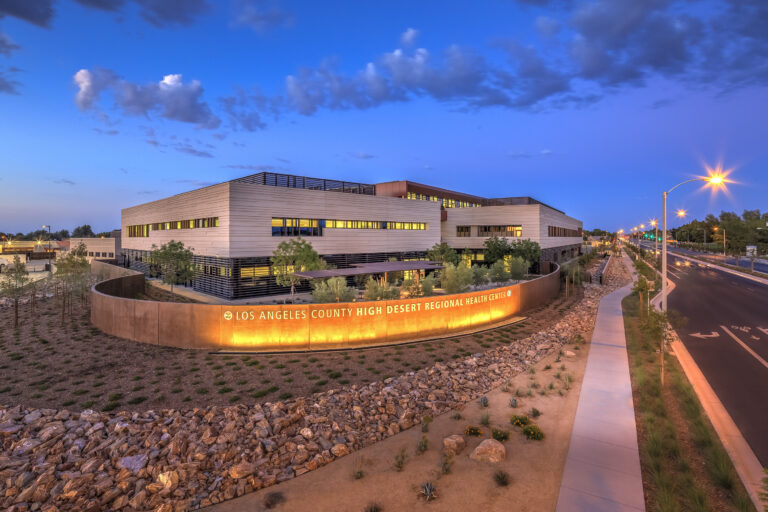 Modern hospital building at dusk with a lit sign reading Los Angeles County High Desert Regional Health Center