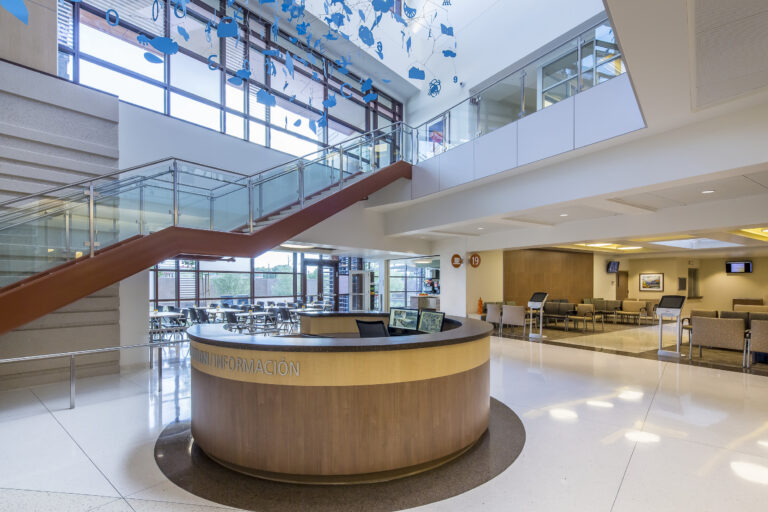 Modern hospital lobby with a circular information desk, staircase, waiting area, and hanging blue artwork