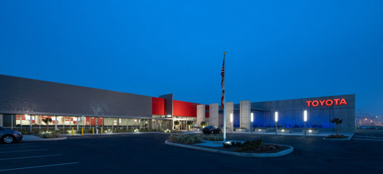 Modern Toyota building at dusk with illuminated sign, flagpole, and empty parking lot