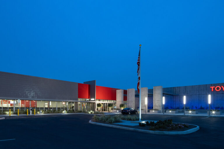Modern Toyota building at dusk with illuminated sign, flagpole, and empty parking lot