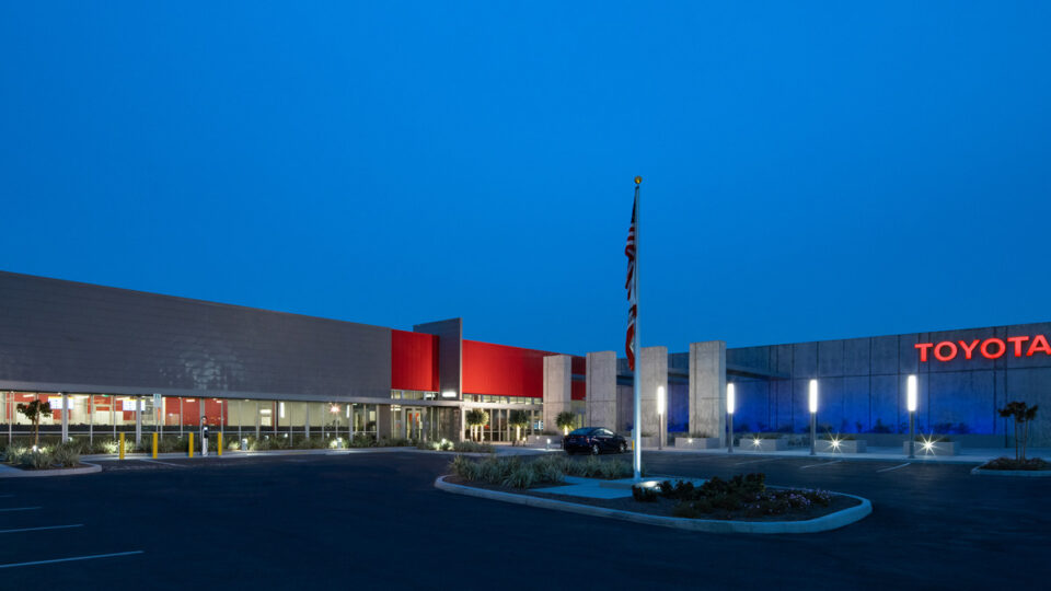 Modern Toyota building at dusk with illuminated sign, flagpole, and empty parking lot