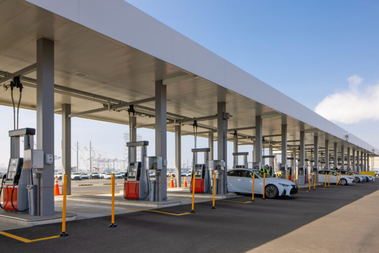 Covered car fueling station with several white sedans lined up at pumps under a large canopy