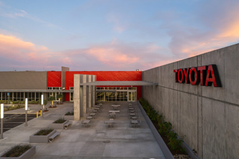 Modern Toyota building courtyard with outdoor tables, concrete walls, and a colorful sunset sky