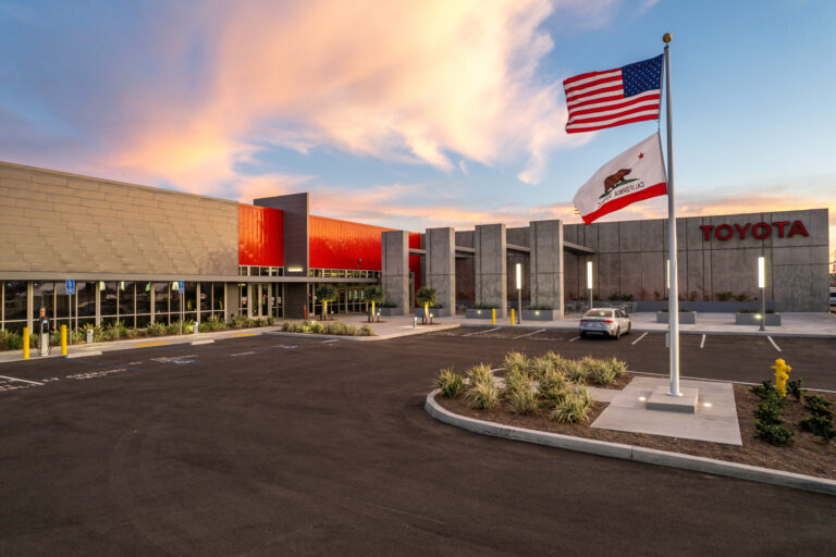 Toyota building exterior at sunset with American and California flags in front of a mostly empty parking lot