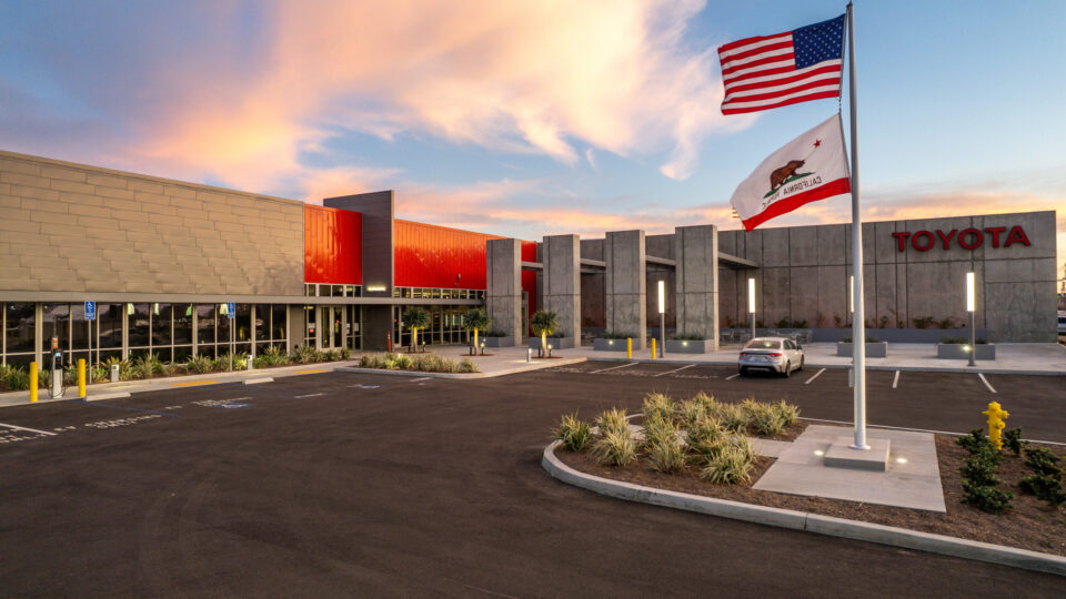 Toyota building exterior at sunset with American and California flags in front of a mostly empty parking lot
