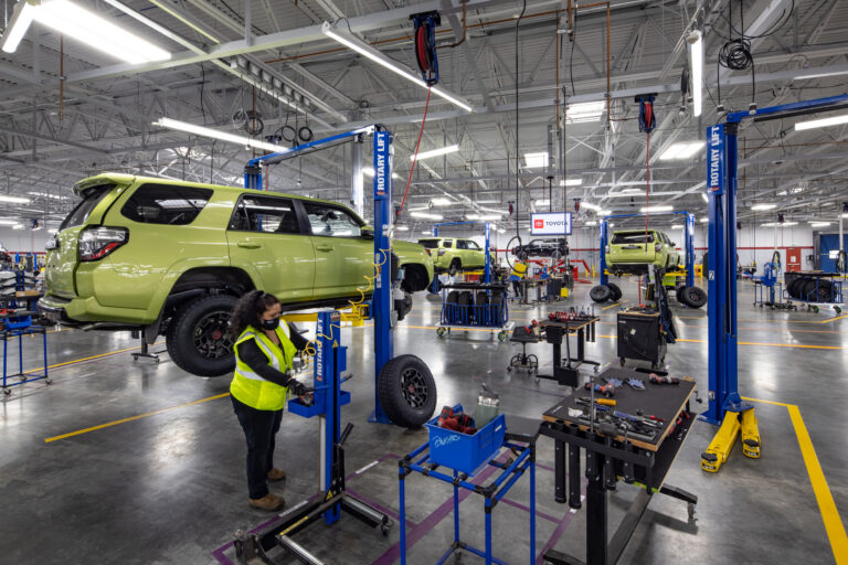 Automotive repair shop with lifted lime-green SUVs, tools, and a worker in a safety vest