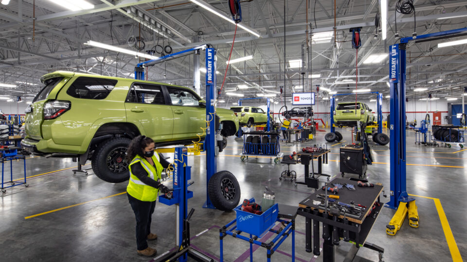 Automotive repair shop with lifted lime-green SUVs, tools, and a worker in a safety vest