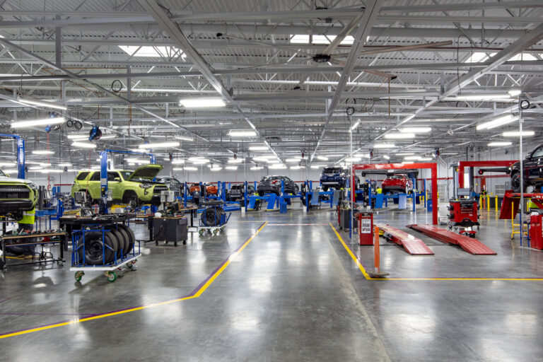 Automotive service shop with multiple cars and SUVs on lifts, tools, and mechanics working under bright ceiling lights