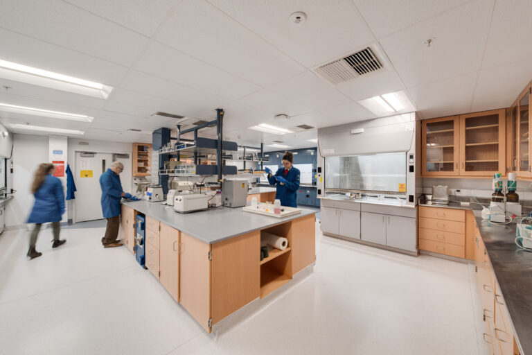 Scientists in blue lab coats working in a modern laboratory with central benches and fume hoods