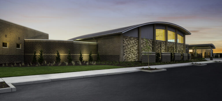 Modern brick building with a curved roof at sunset, beside a paved road and landscaped lawn