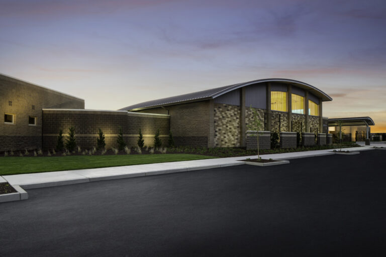 Modern brick building with a curved roof at sunset, beside a paved road and landscaped lawn